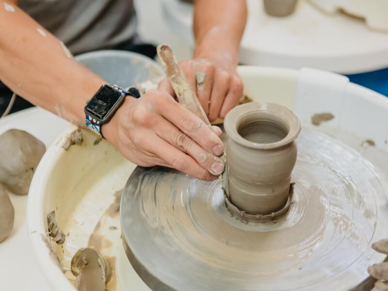 close up of shaping a clay vessel with a tool on a potters wheel